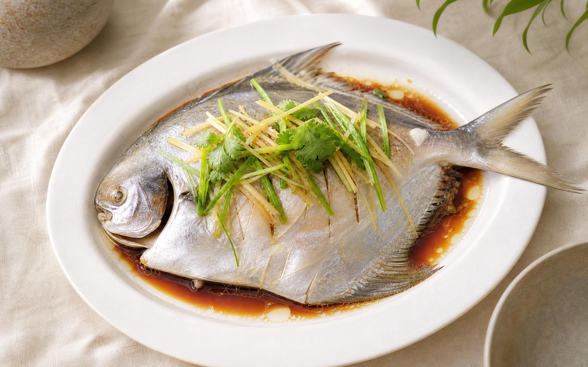 Steamed pomfret with ginger, spring onion and soy on a ceramic platter